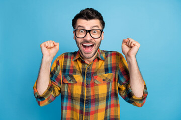 Fototapeta premium Photo of impressed astonished ecstatic man wear glasses plaid shirt hold hands up screaming yes isolated on blue color background