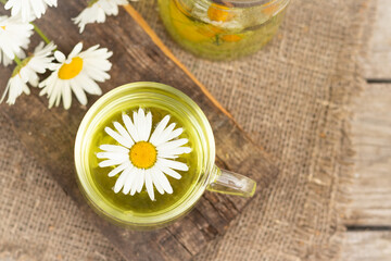 Obraz na płótnie Canvas chamomile tea is a therapeutic healthy drink a cup against the background of daisies A lot of daisies on the table Copy space