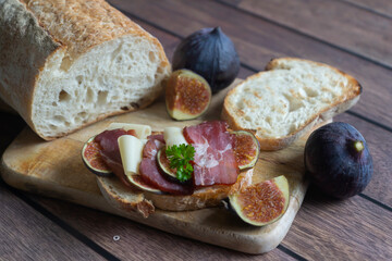 Fresh ciabatta with cheese, figs, bacon and arugula on a dark background.