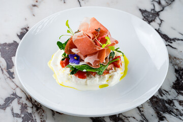 burrata cheese with Italian delicatessen salad with parma ham slices on white plate