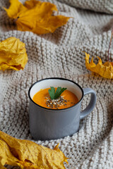 pumpkin soup in a bowl.Pumpkin cream soup in a grey cup on a knitted white background. Vegetarian autumn soup. copy space. vertical. Mug of tasty Pumpkin soup with yellow leaves.