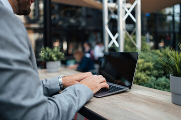 Middle age businessman sitting in cafe bar and enjoying at coffee break between two meetings. He uses laptop computer and he is positive and confident.