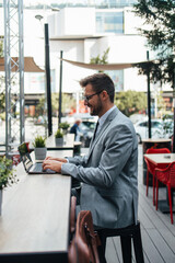 Middle age businessman sitting in cafe bar and enjoying at coffee break between two meetings. He uses laptop computer and he is positive and confident.