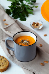 pumpkin soup in a bowl on the table.Pumpkin cream soup in a grey cup with pieces and seeds of pumpkin with green on a white background. Vegetarian autumn soup with croutons. copy space.