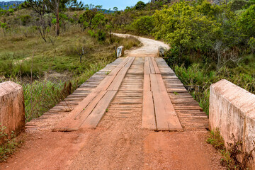 Dirt road with rustic and primitive wooden bridge between hills and the vegetation of the Biribiri environmental reserve in Diamantina