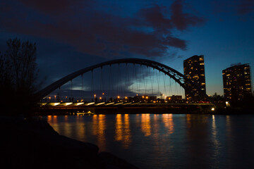 Evening city - arch suspension bridge, night lights, people walking and beautiful evening sky