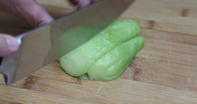 Adult female hands cutting a chayote with a knife on a wooden cutting board for the kitchen, known as: labu siam, jipang, organically grown vegetables. Healthy homemade food concept