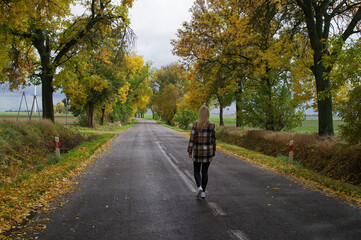 Kobieta idąca ulicą wśród jesiennych drzew.