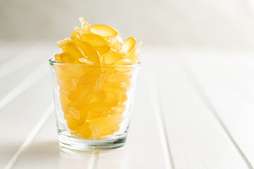Fish oil capsules. Yellow omega 3 pills in glass on white table.