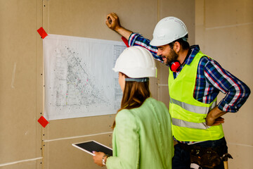 Woman architect and men contractor examining plans on construction site.