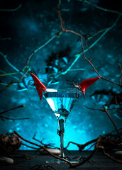 Halloween alcoholic cocktail evil martini on scary dark blue background with twisted branches,...