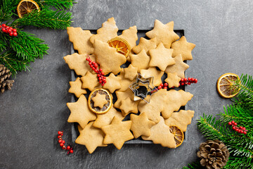 Christmas traditional gingerbread cookies on a plate with decoration, spices and christmas tree branches on dark background. Top view.