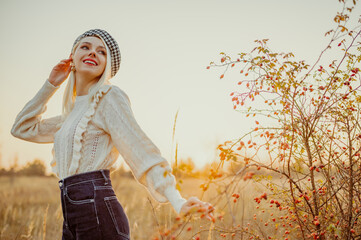 Happy smiling fashionable woman wearing trendy knitted sweater, jeans, houndstooth print beret, posing in beautiful autumn nature during the sunset. Copy, empty space for text