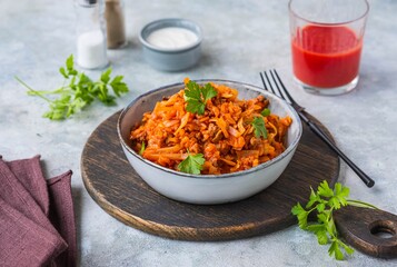 Lazy cabbage rolls, a thick stew of cabbage, carrots, rice and minced meat in a gray ceramic bowl on a gray concrete background.