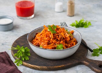 Lazy cabbage rolls, a thick stew of cabbage, carrots, rice and minced meat in a gray ceramic bowl on a gray concrete background.