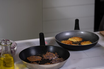 two pans with fried scones on the stove, blurred kitchen in the background, bottle with oil