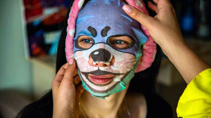 Young girl with facial mask looking at camera over interior background. Cosmetic procedure. Beauty spa and cosmetology.