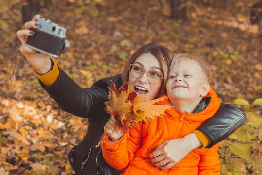 Son and mother are taking selfie on camera in autumn park. Single parent, leisure and fall season concept.
