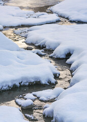River water flowing near ice and snow covered stones, closeup detail