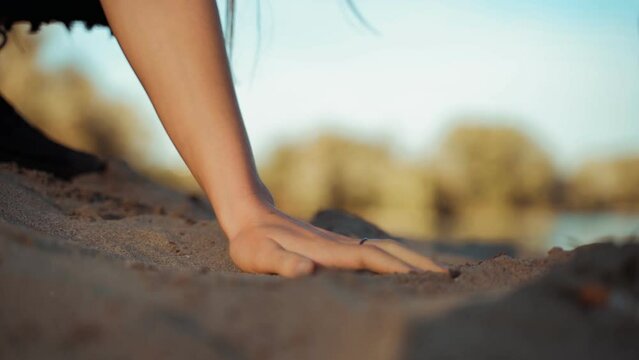 Close up on hand of woman who collects grains of sand from the beach on a sunny day, detail of the sand of the river, sea and lake. Concept of tact and caution