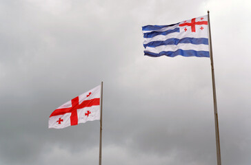 Flag of Georgia and Adjara against the sky with thunderclouds.