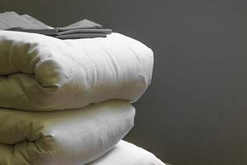 Stack of new clean bedding sheets soft folded blankets and pillows isolated on gray background indoors. Cleaning service