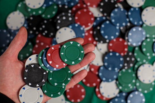 the player holds poker chips. Male casino player holding several chips with a green table and chips on the background, close-up hands. casino, gambling, poker, people and the concept of entertainment.