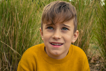 La mirada de un niño pequeño rubio sonriente expresivo en un jardín - obrazy, fototapety, plakaty