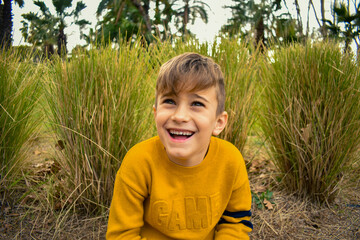 La mirada de un niño pequeño rubio sonriente expresivo en un jardín - obrazy, fototapety, plakaty