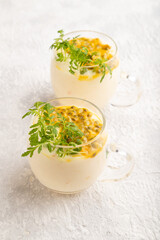 Yogurt with passionfruit and marigold microgreen in glass on gray. Side view.