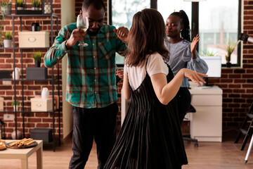 African american couple dancing, enjoying social life accompanied of young adult caucasian girl at diverse friends party. Various nationalities people drinking wine, having fun.