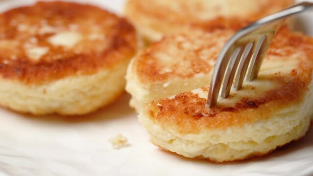 Appetizing cheese pancake is pierced with fork and cut with knife. 