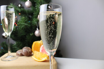 New Year's still life champagne in a glass against the background of a green Christmas tree and citrus orange and grapefruit on a tray of wood. New Year holiday atmosphere