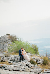 Groom hugs bride sitting on the stone top of the mountain