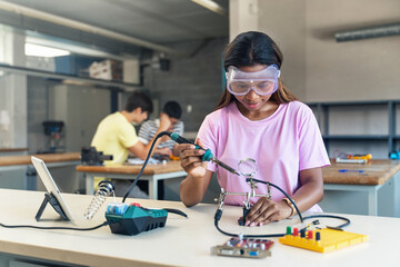African American High School teenage Student wearing protective goggles soldering electronics...