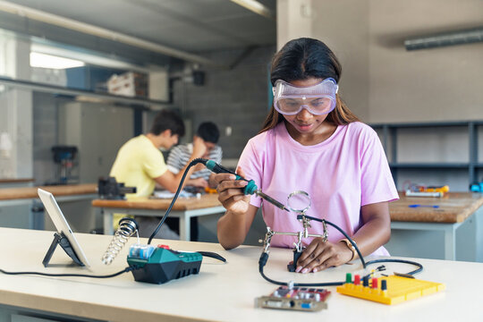 African American High School Teenage Student Wearing Protective Goggles Soldering Electronics Circuit In The Science Technology Workshop - Digital Innovation In Education