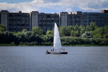 A sailing boat on the river, among the city buildings. Sailing trip. Landscape with a sailing boat on the river, against the background of the factory.