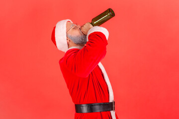 Side view of drunk elderly man with gray beard wearing santa claus costume celebrating winter...