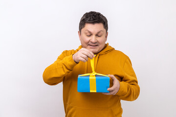 Middle aged man opening gift box, unwrapping birthday present for celebrating holiday, pulling ribbon, looking at gift, wearing urban style hoodie. Indoor studio shot isolated on white background.
