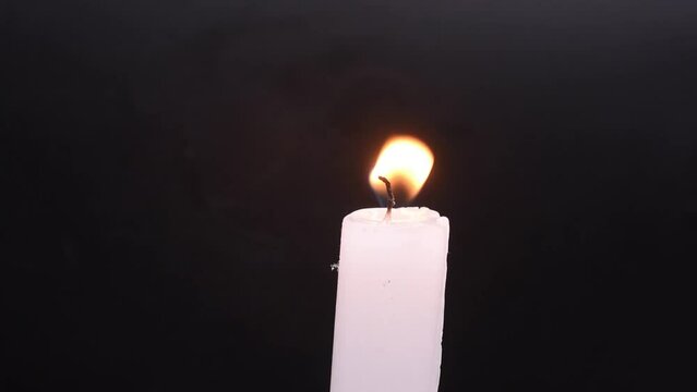 Vela de cera tipo altar encendida en un fondo negro 