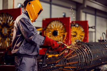 Fototapeta A metallurgy worker welds metal framework with a welding machine in the factory. obraz