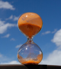 Hourglass timer with orange sand and blue sky with soft clouds in the background