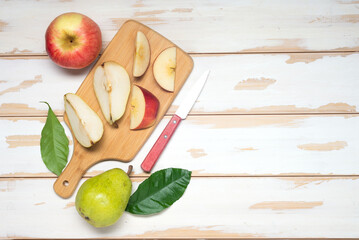 pieces of pears and apples on a cutting board with a knife. White boards table, top view. Space for text