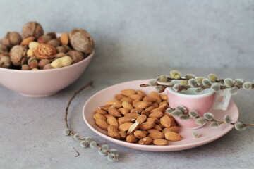 Almonds on a pastel pink plate, composition on a gray background with empty space for text, tasty vegan / vegetarian snack, healthy low calorie diet concept.