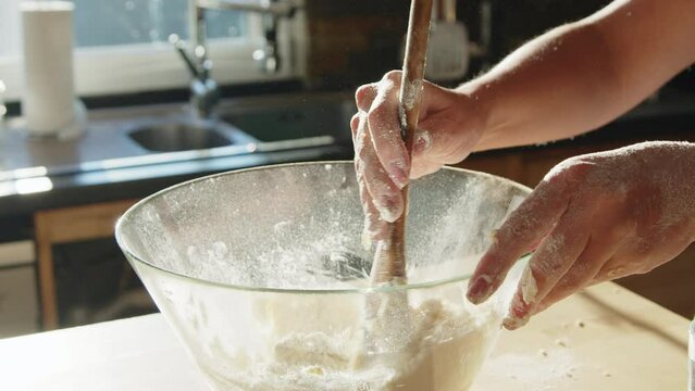 Woman is making dough at home, mixing the ingredients with wooden spoon, preparing some tasty baking, beautiful close up shot, slow motion.