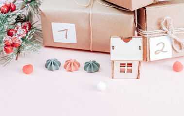 Craft gifts with numbers 1, 2, tied with a jute thread, a spruce branch, a wooden house and cookies on a pink background.
