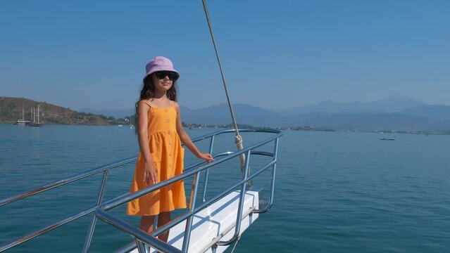 Child on deck during a boat trip. A view of happy little girl relax on the modern floating yacht in the sea. A concept of sailing trip in the calm blue bay water.