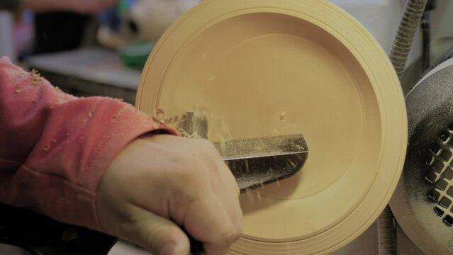 Man carpenter using gouge for shaping piece of wood on turning lathe machine with many shavings flying in camera at workshop - close up. Carpentry, woodworking, craftsmanship and manufacturing concept