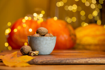 Autumn decoration on wooden table with ceramic bowl full of walnuts and pumpkins