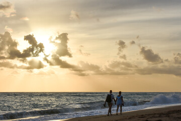 Young couple hand to hand walking on a beach at cloudy sunset